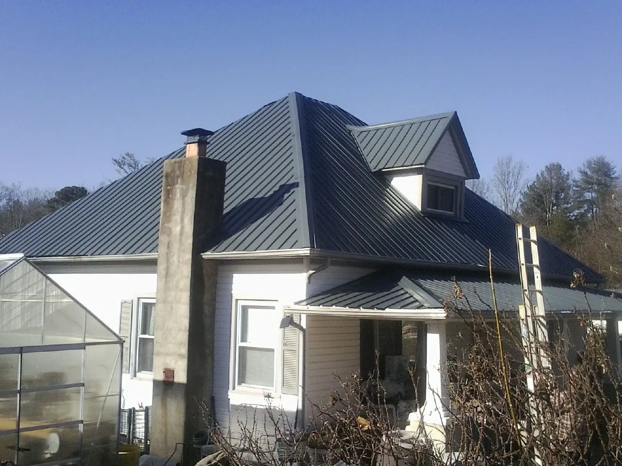 Dark blue standing seam metal roof on a white farmhouse with dormer — Slate & Tile Roof Repair by Roofing Brothers in Lengby