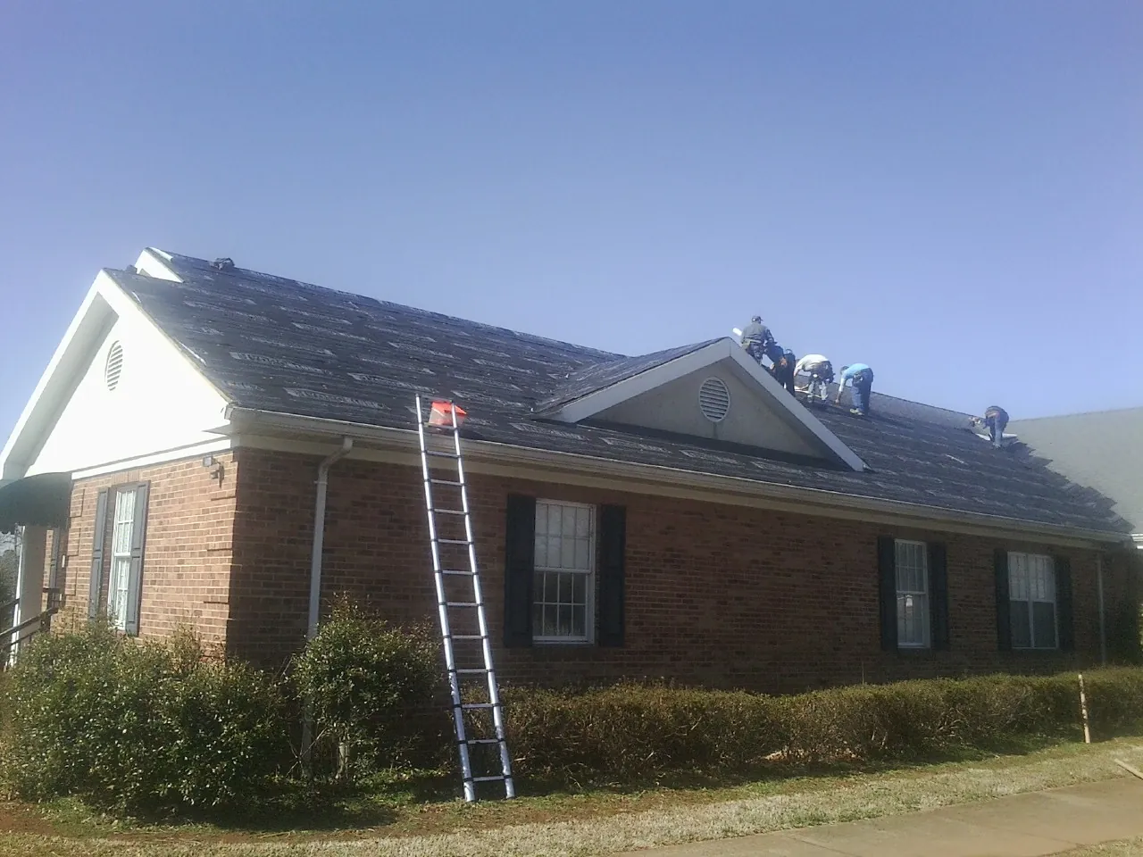 Crew tearing shingles off a brick ranch roof with a ladder set — Emergency Roof Repair work by our crew in Lengby