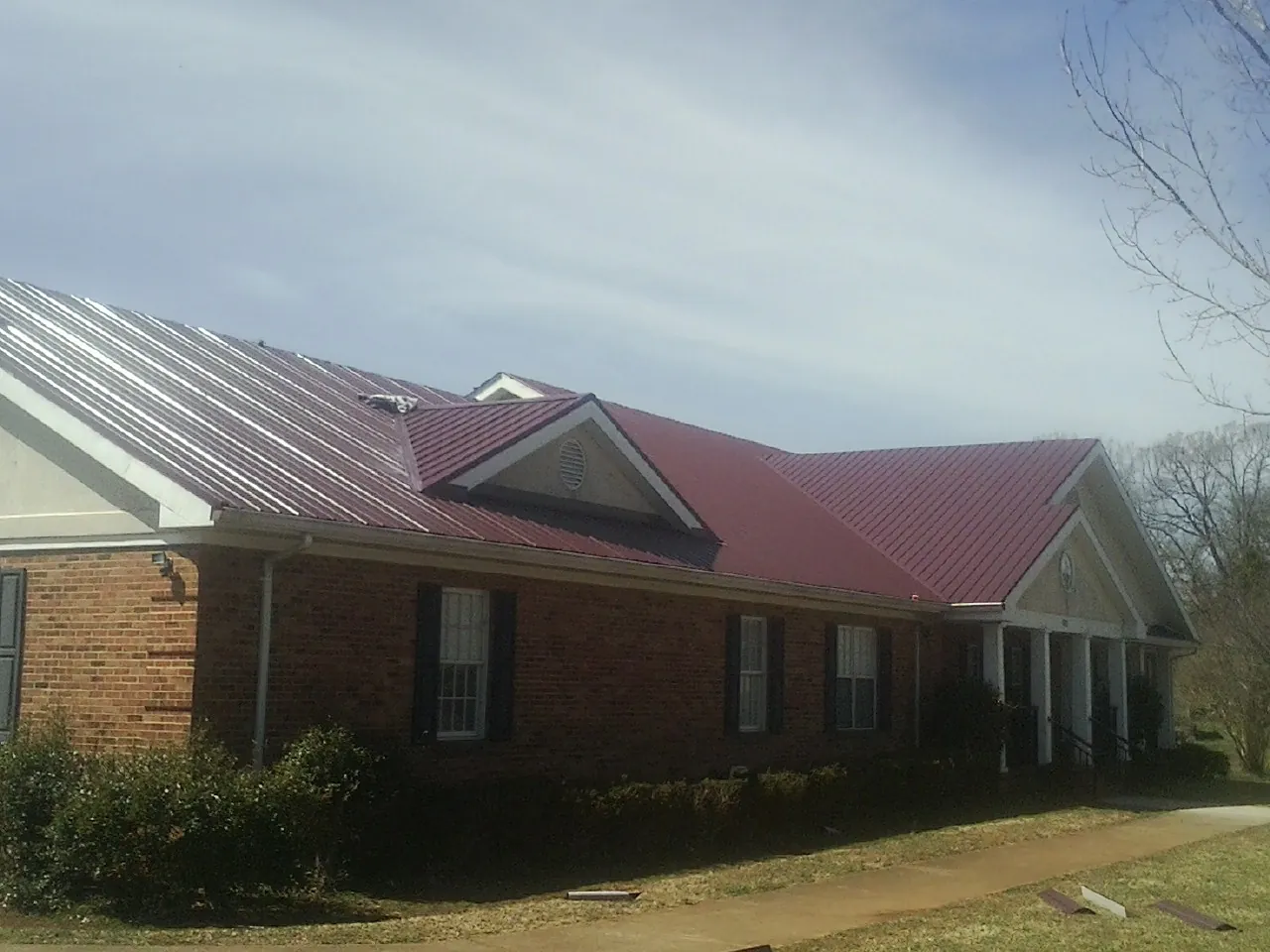 Red metal roof with gabled entries on a long brick building, from a Hail Damage Roof Repair job in Lengby