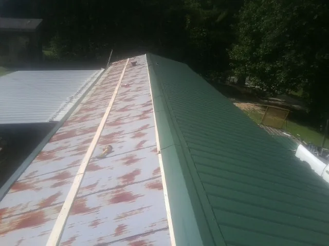 Old rusted panels beside newly installed green metal roofing — Wind Damage Roof Repair by Roofing Brothers in Lengby