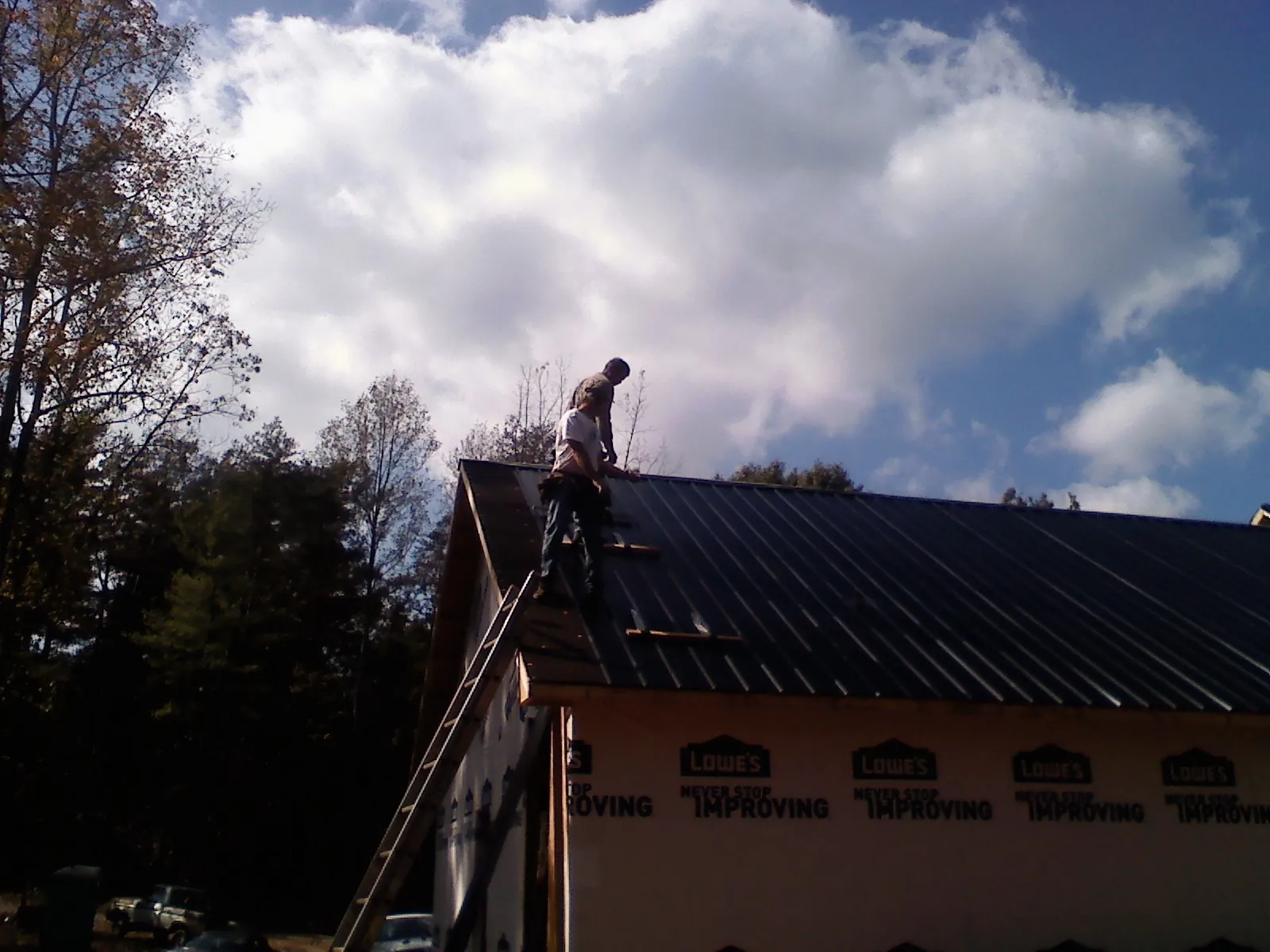 Roofer fastening dark metal panels high against a cloudy sky, from a Roof Inspection job in Lengby
